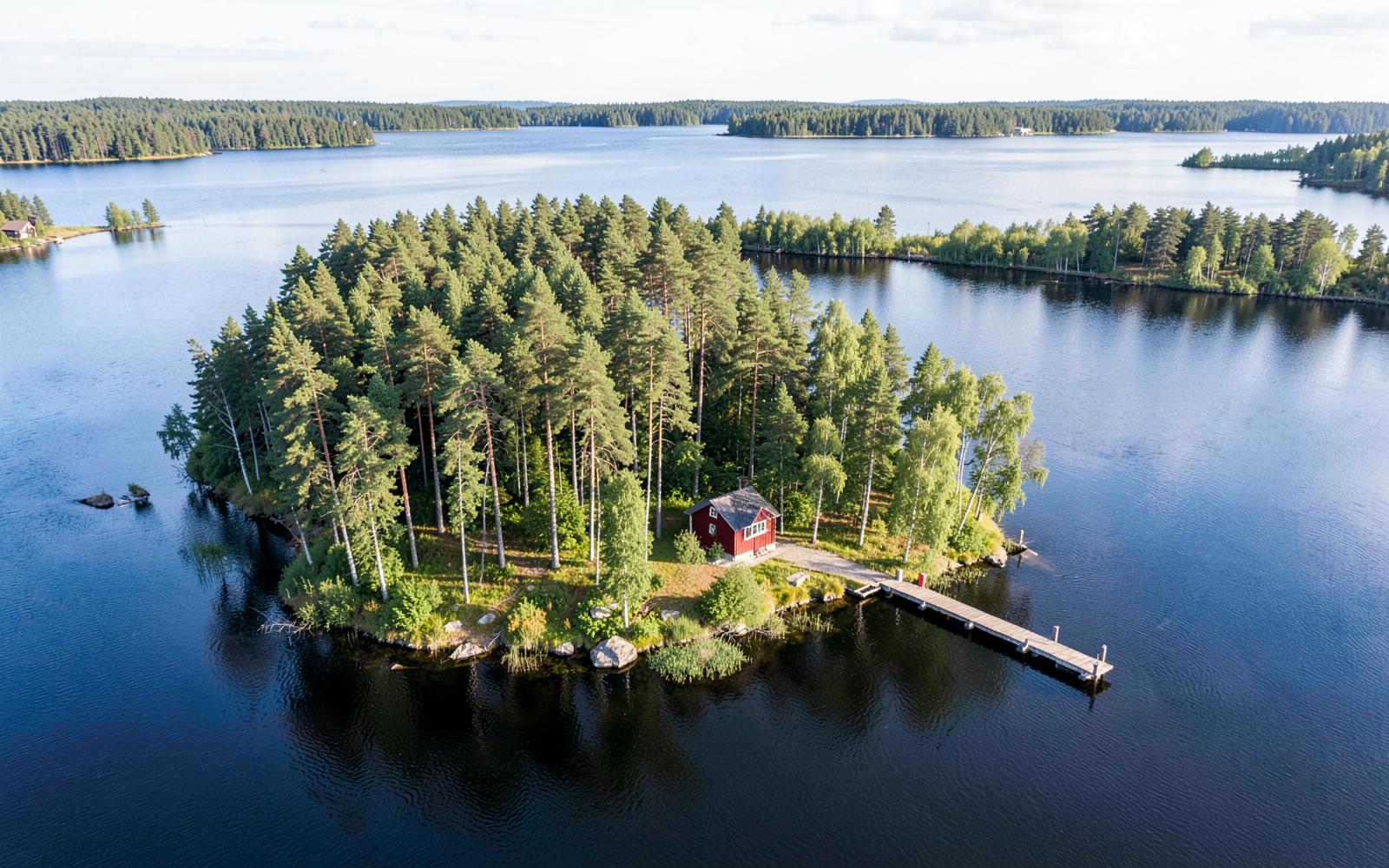 Forested private island for sale on a freshwater lake in Finnish Lakeland with a red cabin and jetty